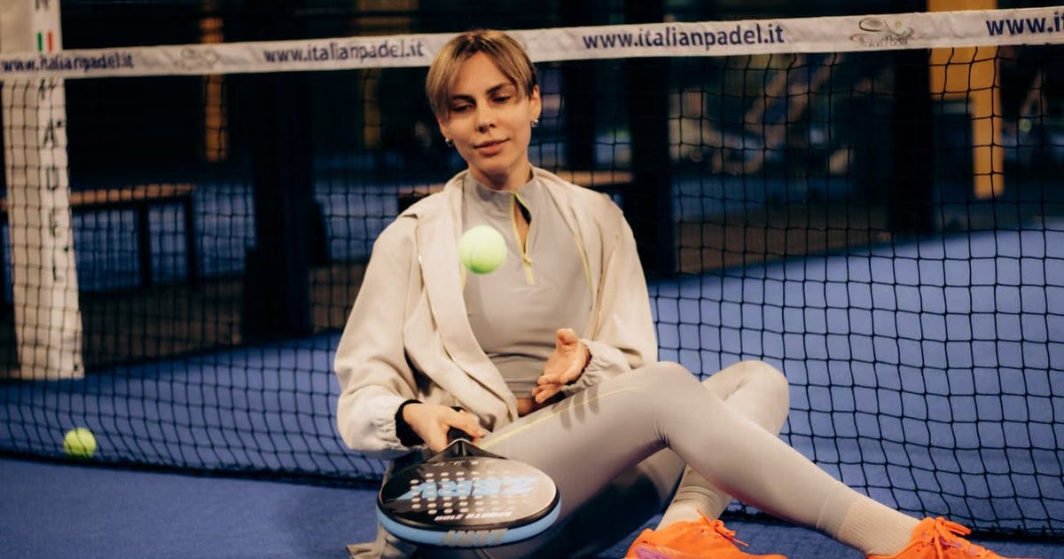 Female player sitting on indoor padel court with gear after match.