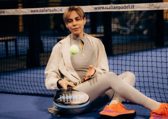 Female player sitting on indoor padel court with gear after match.