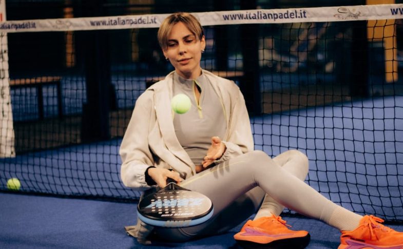 Female player sitting on indoor padel court with gear after match.