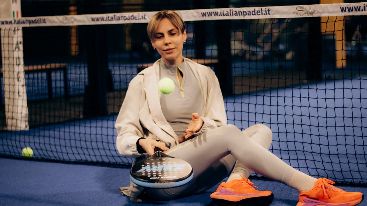 Female player sitting on indoor padel court with gear after match.